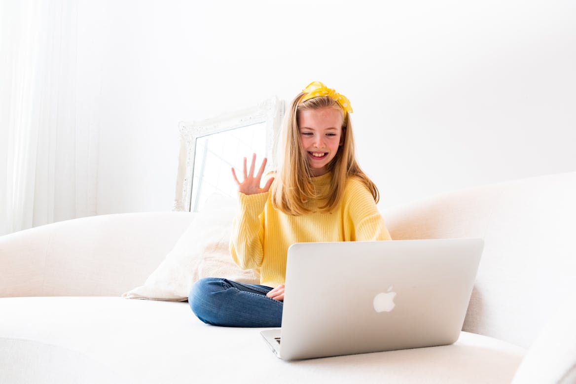 Girl wearing yellow waving hello to others on a laptop Girl wearing yellow waving hello to others on a laptop