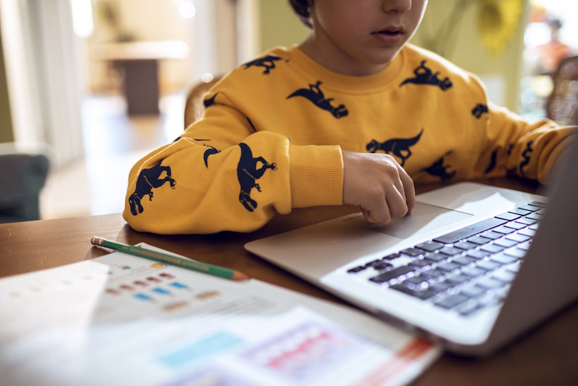 Boy wearing a yellow sweater cropped out with a workbook open next to a laptop Boy wearing a yellow sweater cropped out with a workbook open next to a laptop