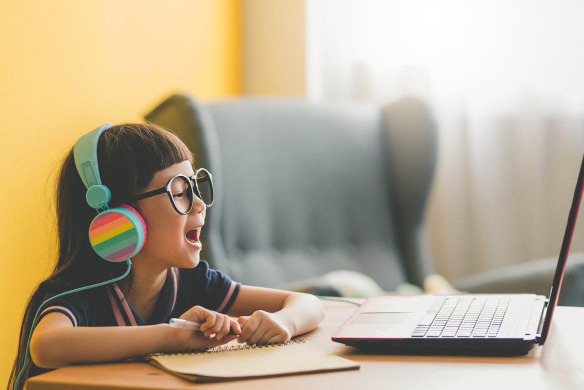 Girl with glasses writing in front of a laptop with rainbow headphones Girl with glasses writing in front of a laptop with rainbow headphones
