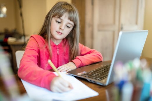 Girl in bright colored jacket writing on some paper next to a laptop