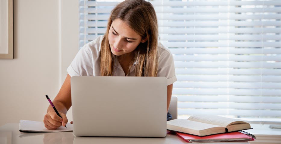 Teenage girl writing in a notebook with a computer and books open Teenage girl writing in a notebook with a computer and books open