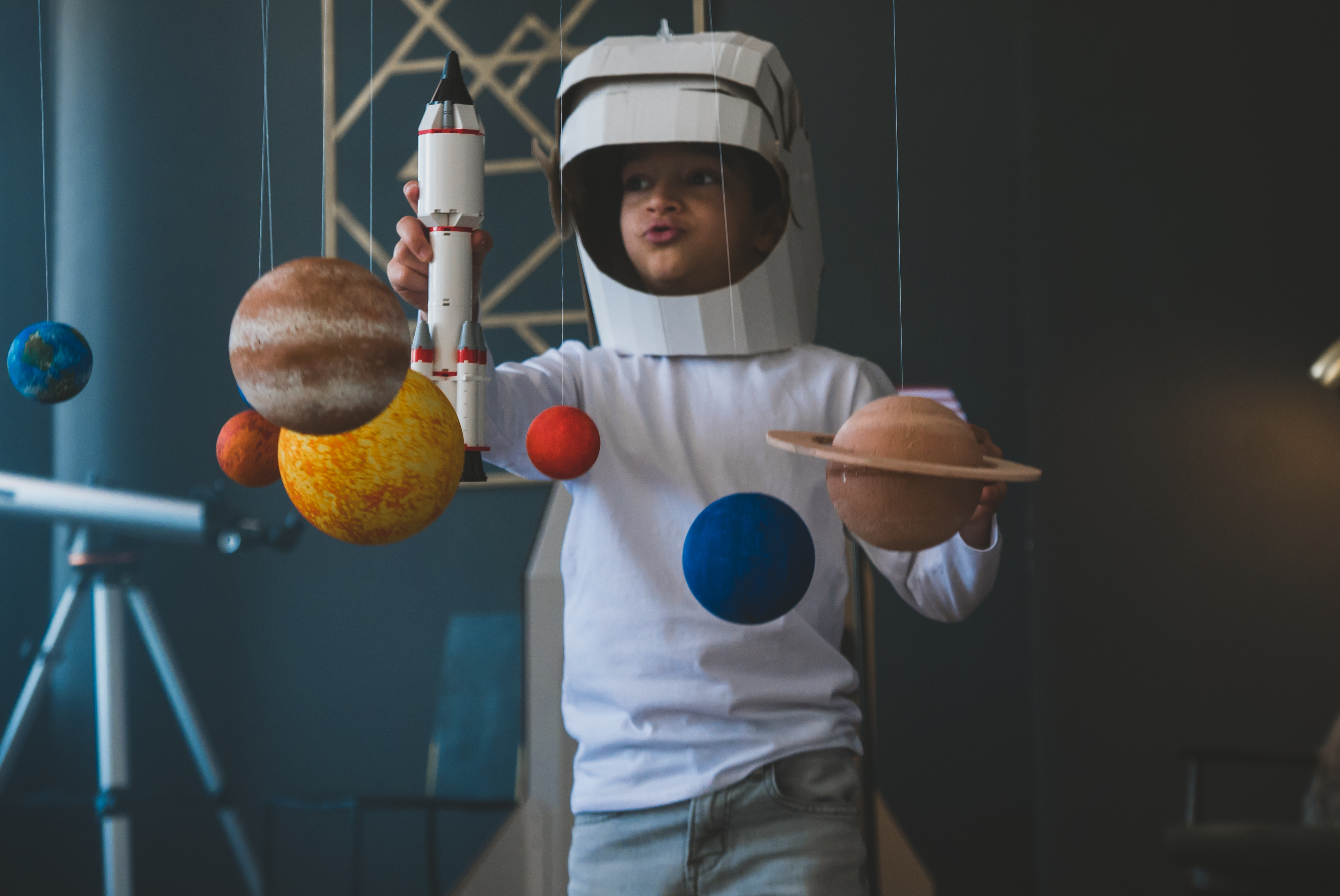 School-aged child in homemade space costume playing with rocket ship and solar system diorama