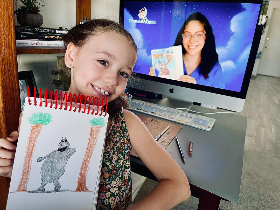 Girl holding up her drawing in front of a computer
