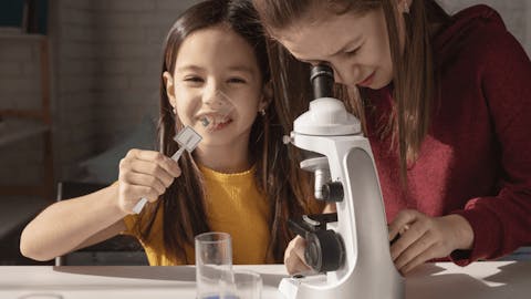 School-aged girls engaging in science experiment using microscope School-aged girls engaging in science experiment using microscope