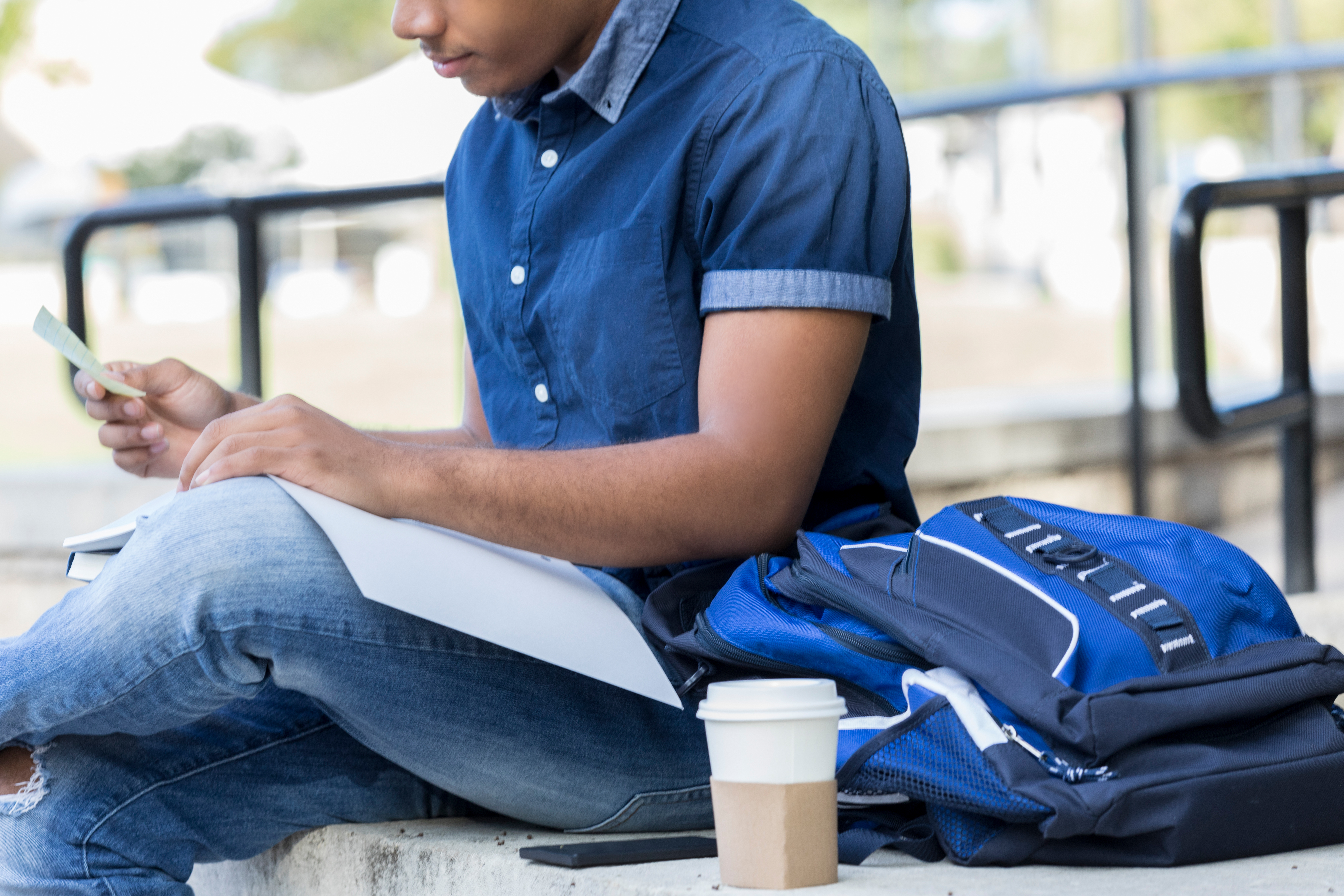 Man with flashcards, book, and coffee studies on a bench