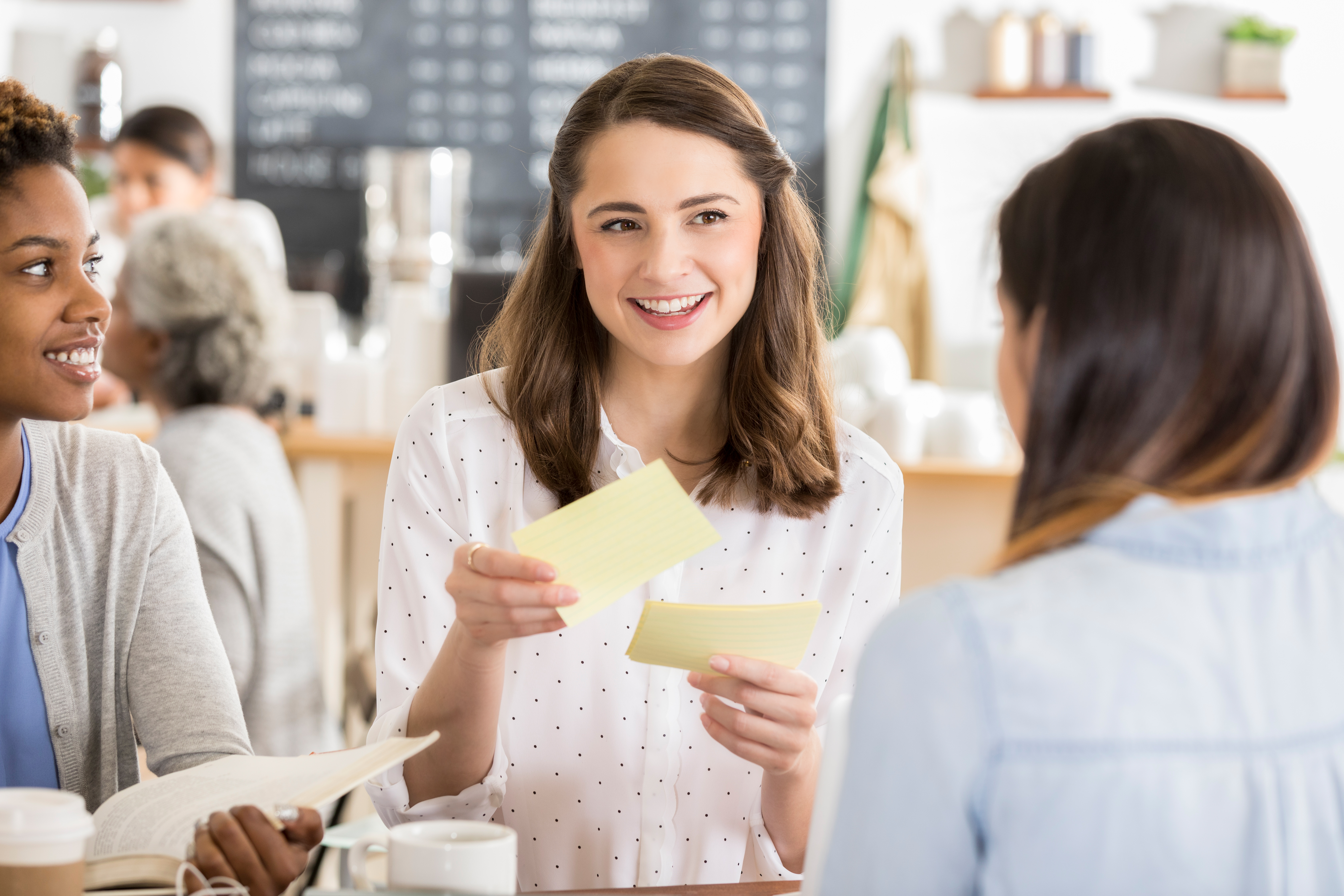 Woman uses flashcards to study while at a coffee shop with two friends