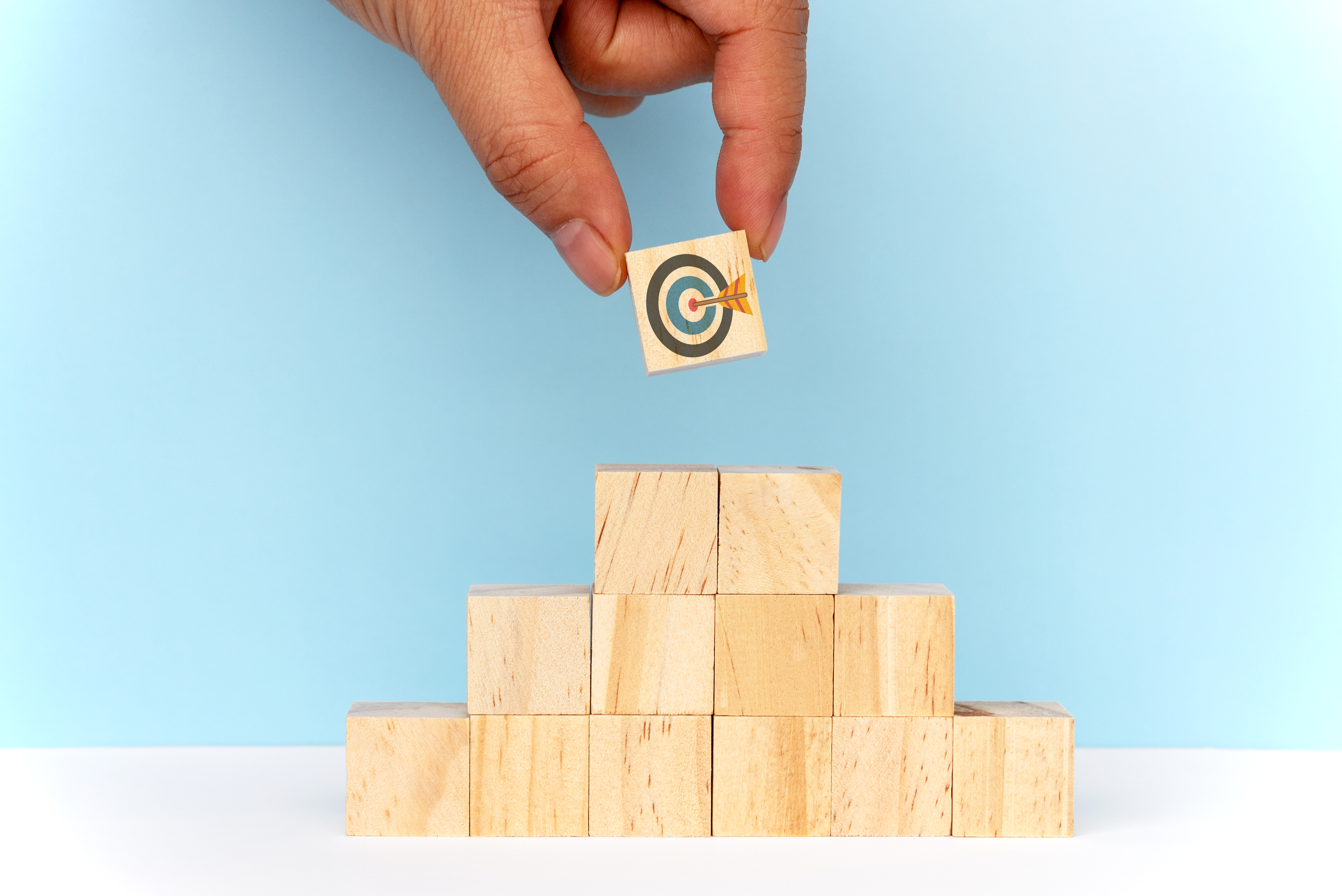 Hand places a block with a target painted on it on top of a block pyramid