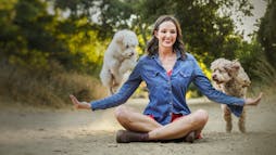 Nicole Ellis from Rover.com sitting on the ground while two dogs jump over her arms Nicole Ellis from Rover.com sitting on the ground while two dogs jump over her arms