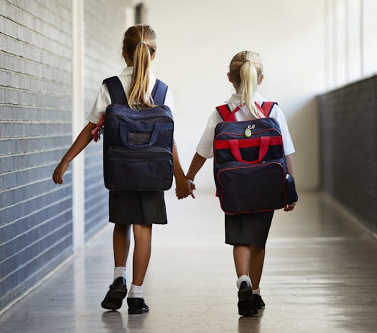 two children with backpacks holding hands walking down a hallway two children with backpacks holding hands walking down a hallway